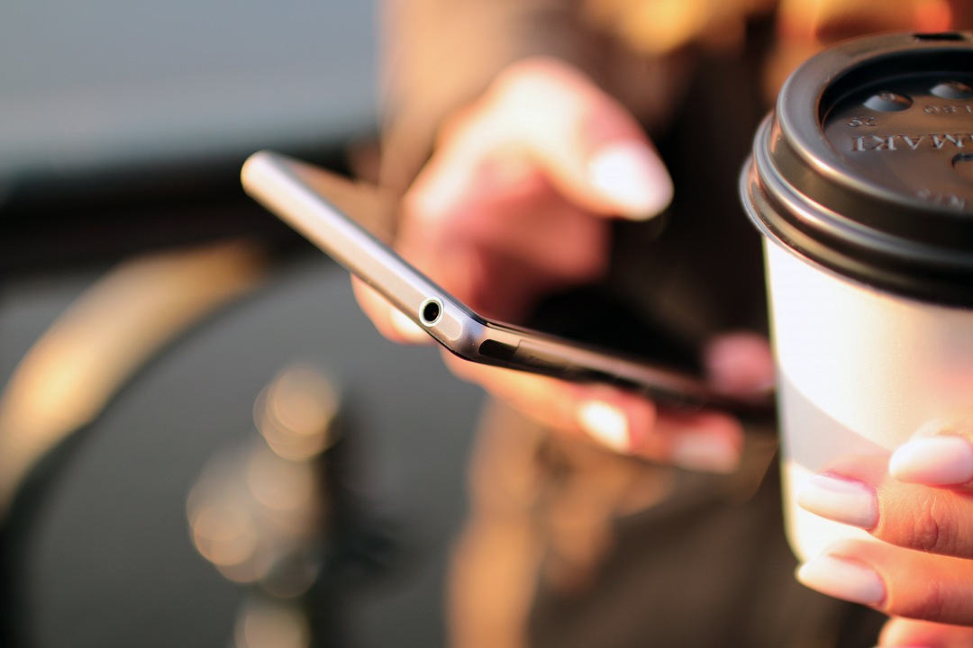 a woman holding a cup of coffee while using her phone