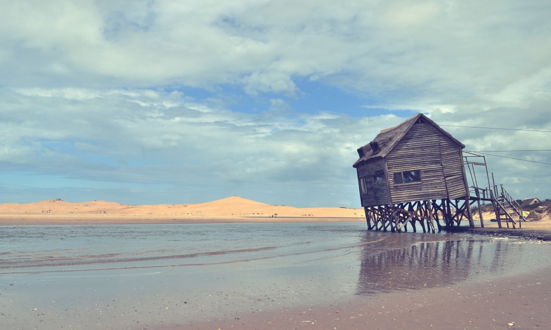 a wooden house on the beach with a cloudy sky