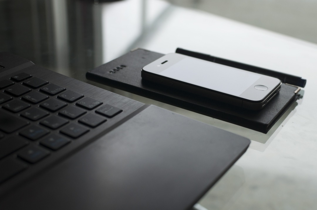 laptop with smart phone on glass table and pen
