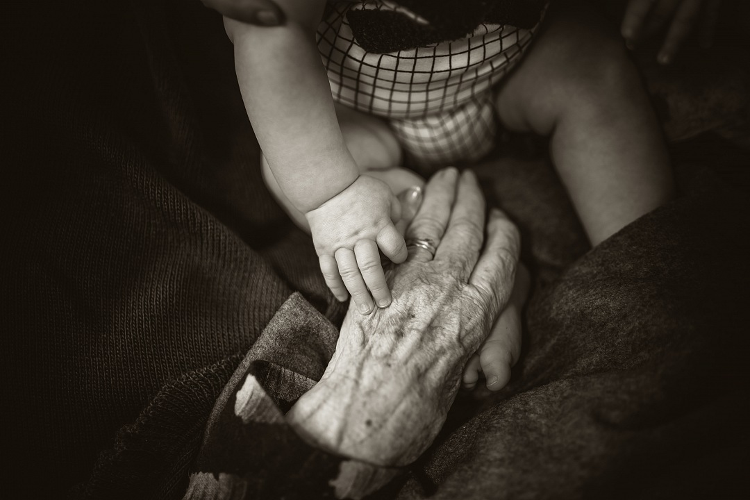 This evocative image captures a poignant moment between generations, featuring an elderly woman holding hands with a younger person while wearing a mask. The scene symbolizes resilience and connection in challenging times, making it an ideal choice for articles and campaigns focusing on family bonds, health awareness, and the emotional impact of social distancing. Perfect for use in healthcare, community support, and intergenerational relationship themes.