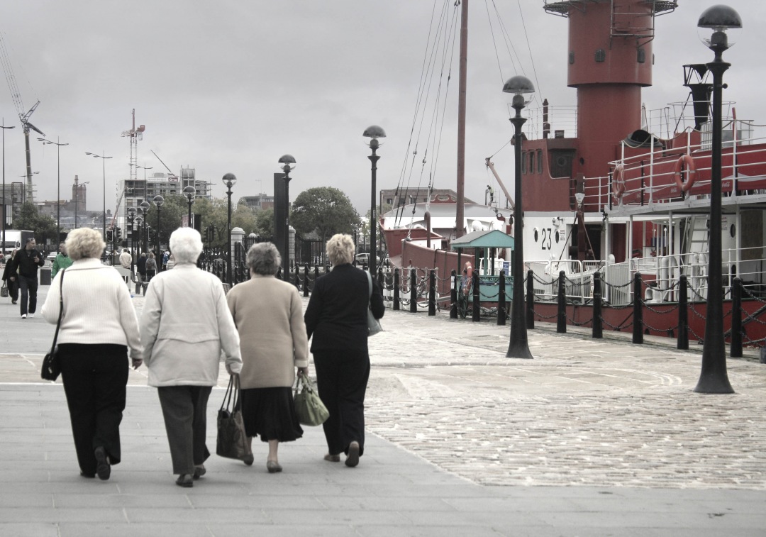 This captivating image features two women leisurely walking down a picturesque street, with a striking red lighthouse standing majestically in the background. The scene evokes a sense of tranquility and companionship, making it perfect for themes related to friendship, travel, and coastal adventures. Ideal for use in travel blogs, lifestyle articles, or any content that conveys joy and exploration in coastal settings.
